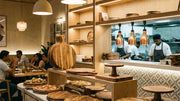 Premium wooden pizza boards, platters and cake stands styled on restaurant tables in a modern Indian café interior with warm beige lighting, showcasing commercial wooden serveware for hospitality.